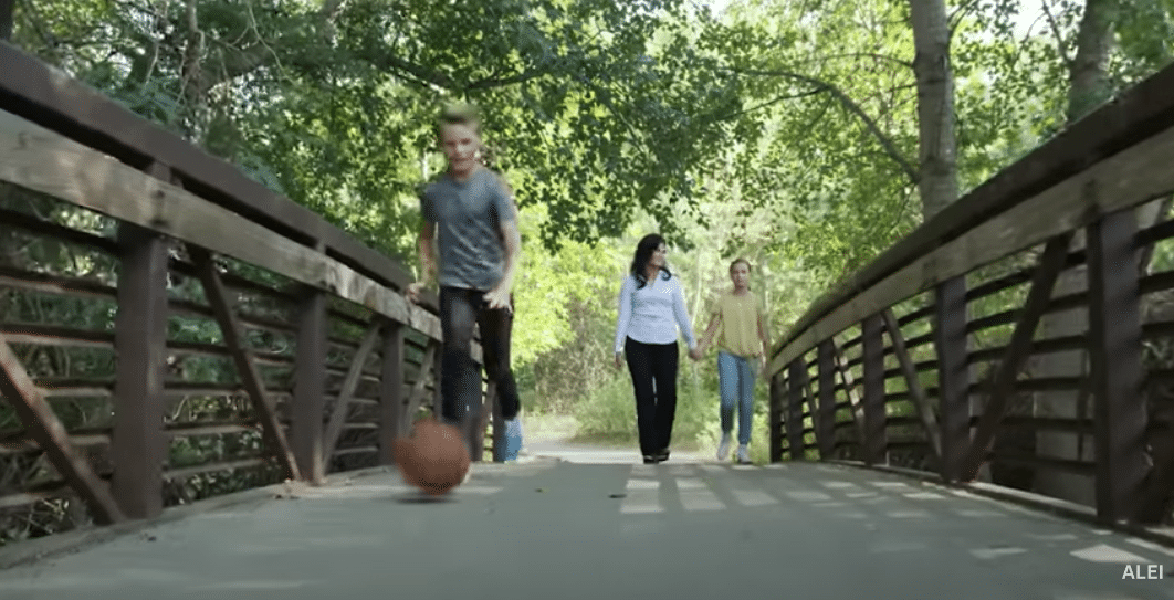 Child and parent walking across a bridge with a basketball rolling on the ground